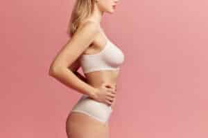 Side profile of a woman in a beige bra and panty set, symbolizing post-pregnancy body rejuvenation through cosmetic surgery.