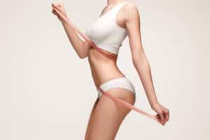 Slim torso of woman measuring waist indicating post-mommy makeover results.