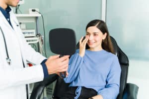 Patient smiling in mirror, reviewing rhinoplasty results with doctor.