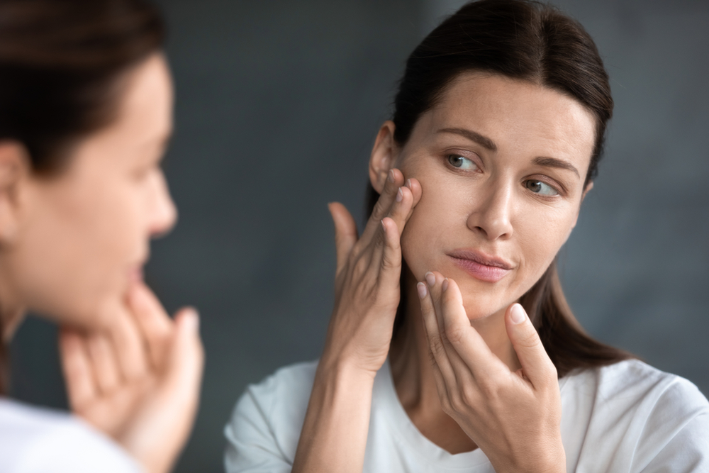 Woman examining potential hyperpigmentation on facial scar in mirror.