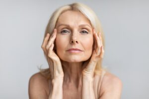 Mature woman touching temples, considering brow lift for hooded eyes rejuvenation.