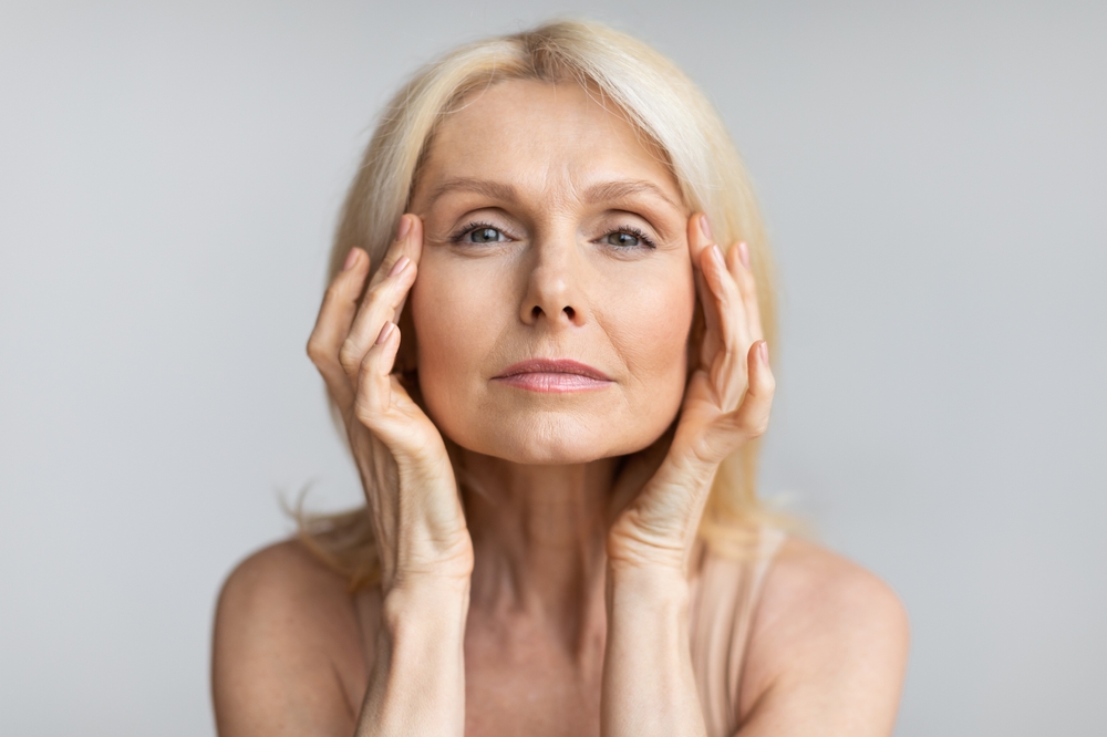 Mature woman touching temples, considering brow lift for hooded eyes rejuvenation.