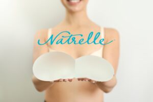 Smiling woman holding Natrelle Gummy Bear breast implants, symbolizing customized choices.