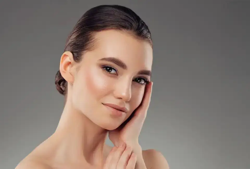 Woman with smooth skin gently touching her face, showcasing the refined results of non-surgical rhinoplasty using dermal fillers for nose enhancement.