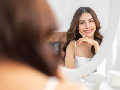 Woman admiring her reflection, considering the costs of buccal fat removal surgery.