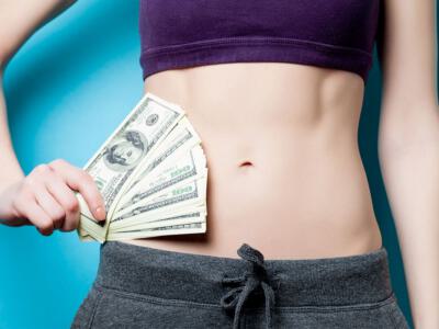 Frontal view of a woman's abdomen while she holds dollar bills in relation to financing options after extra skin removal surgery or body lift surgery.