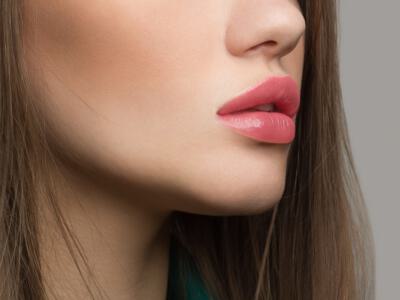 Close-up of a woman's lips slightly parted, highlighted by pink lipstick, demonstrating lip augmentation effects.